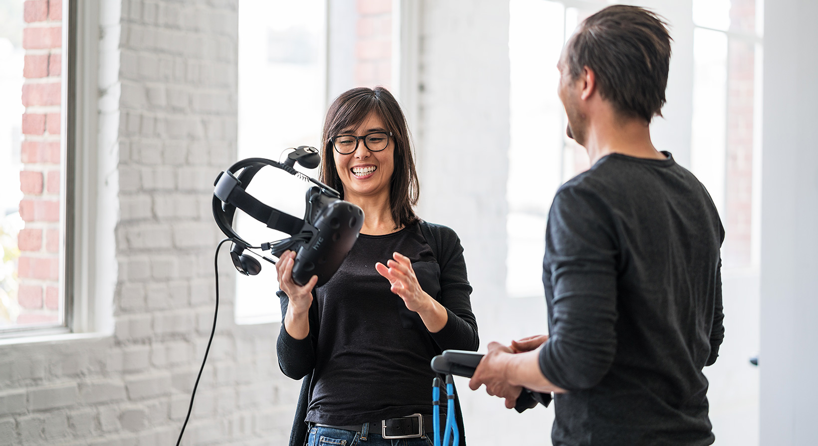 smiling female holding virtual reality headset and discussing with male engineer