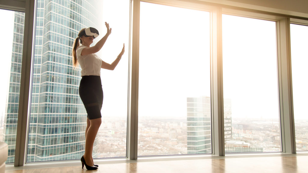 Excited businesswoman wearing headset experiencing real estate virtual tour standing near window